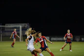 Adults playing a competitive coed soccer match under bright stadium lights.