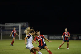 Adults playing a competitive coed soccer match under bright stadium lights.