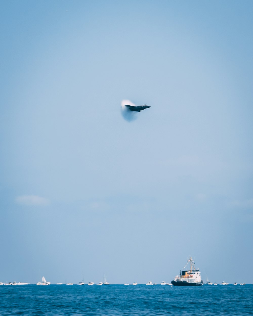 Un avión de combate crea un estampido sónico sobre el mar con barcos