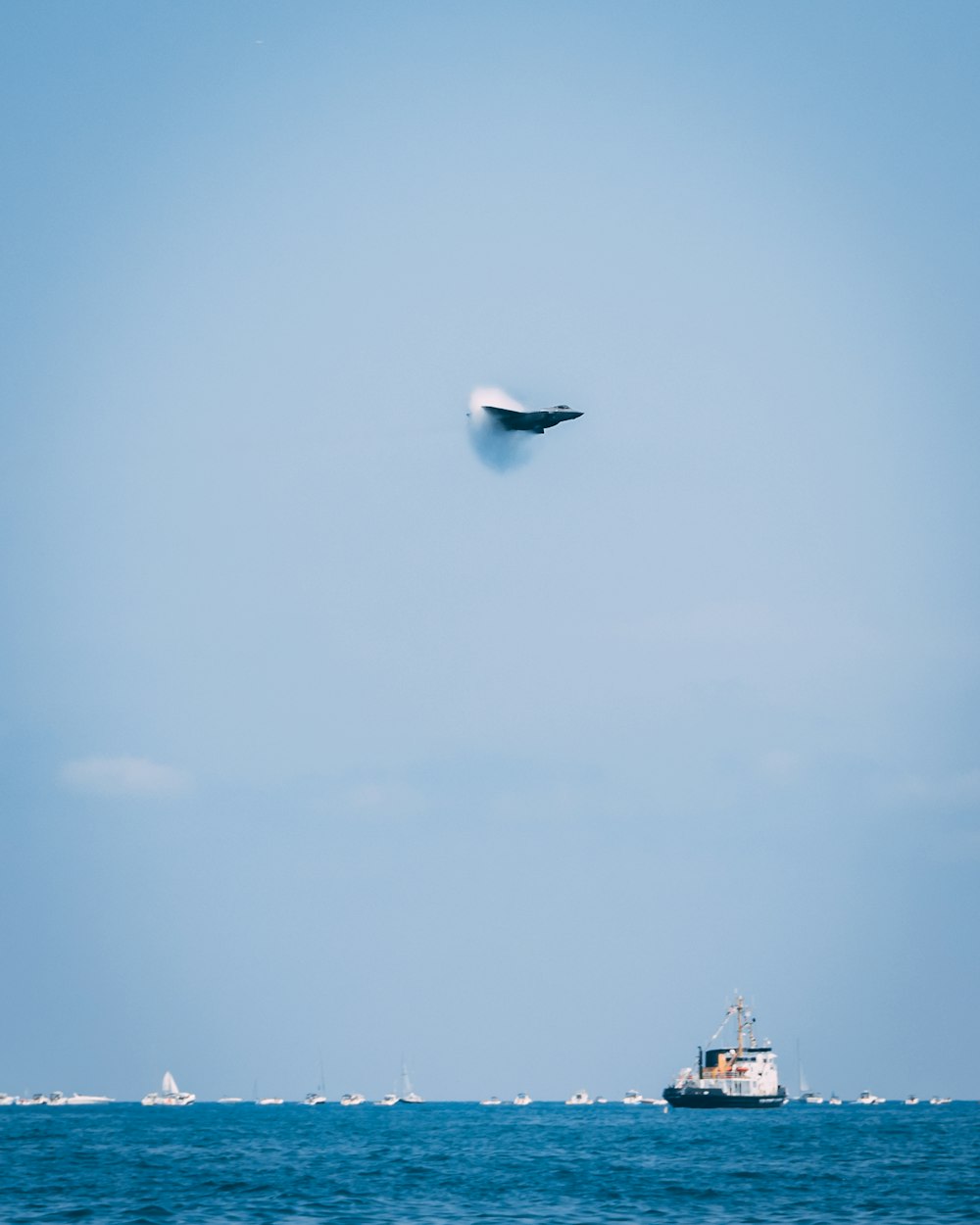 jet fighter creating sonic boom over the sea with ships