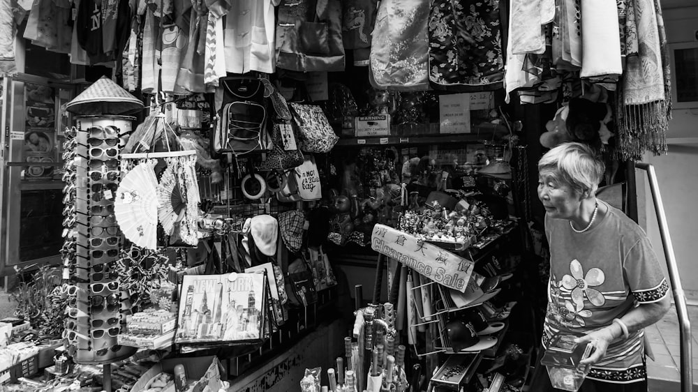 grayscale photography of woman standing beside store