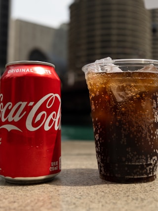 Coca-Cola soda tin can and cup on table close-up photography