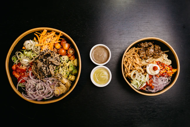 A close-up of various sauces and toppings ready for poke bowls.