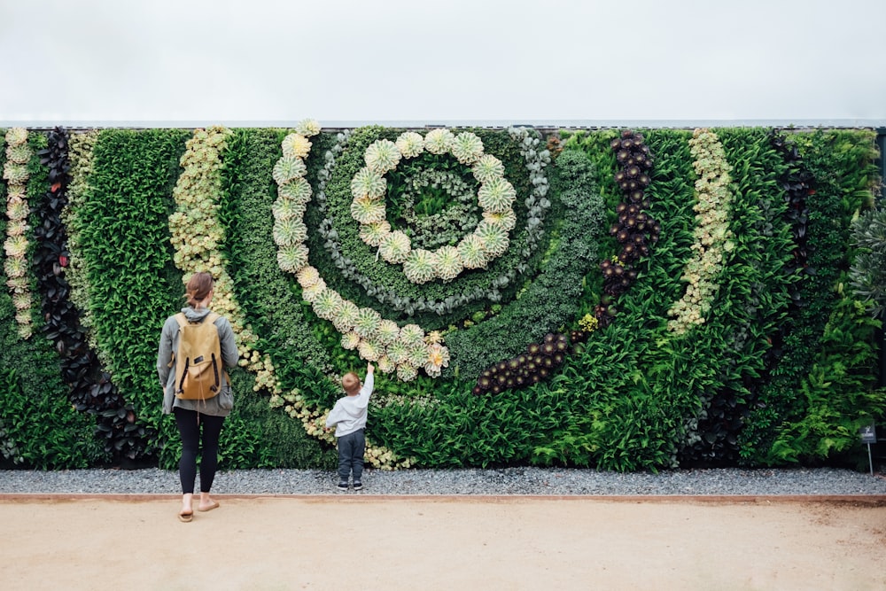 Uma mulher e uma criança estão em frente a um muro verde