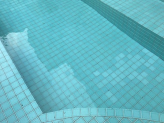 Turquoise mosaic tiles form the surface of a pool or fountain, with shadows and reflections visible on the water.