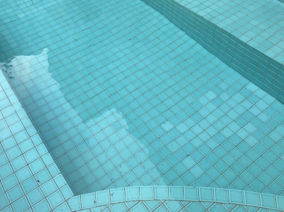 Turquoise mosaic tiles form the surface of a pool or fountain, with shadows and reflections visible on the water.