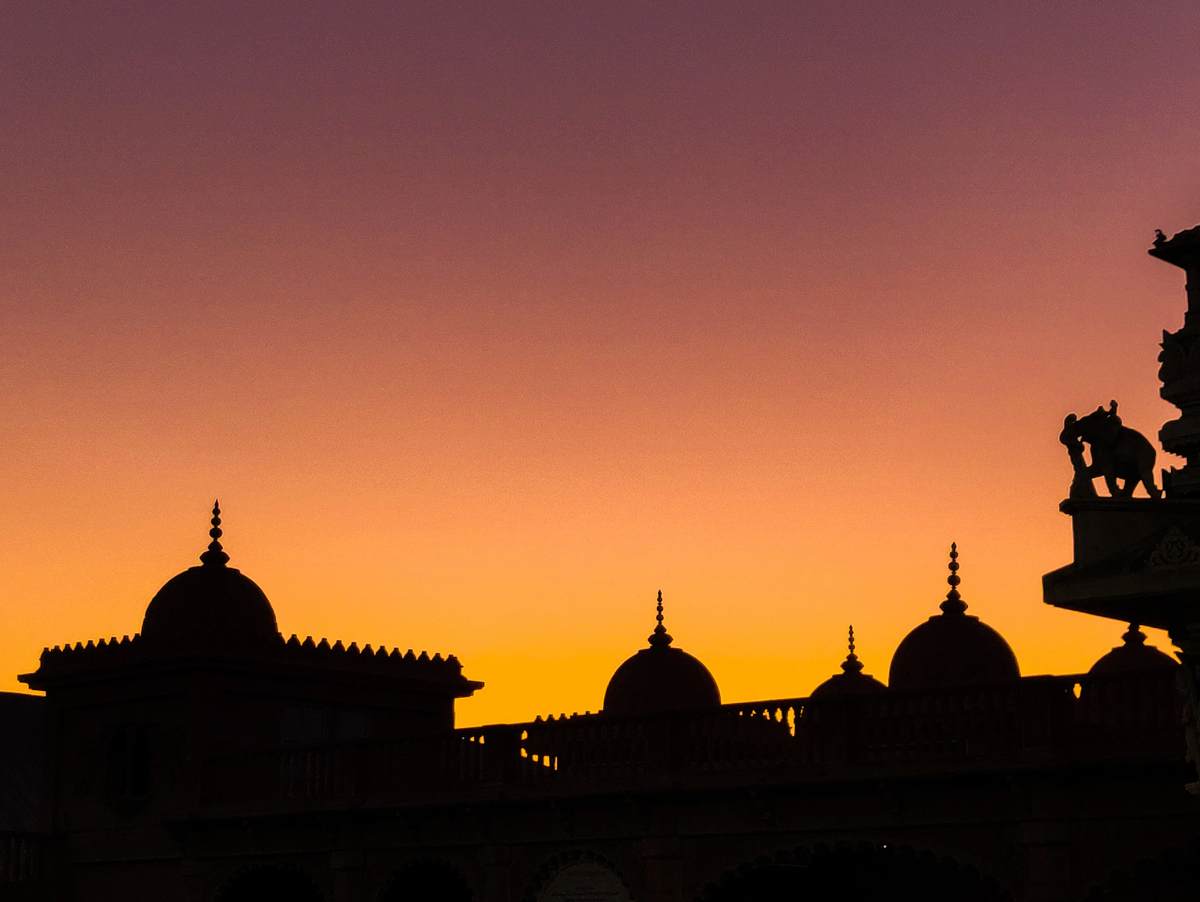 Rajasthani domes and chhatris in silhouette against a deep orange sunset sky