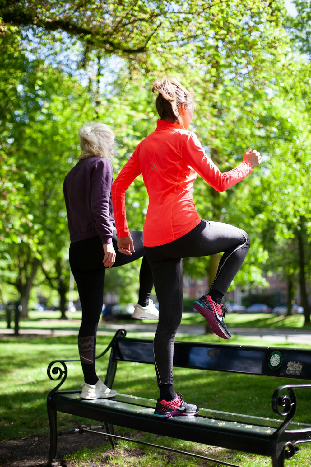 photography of women standing on black bench near outdoor during daytime