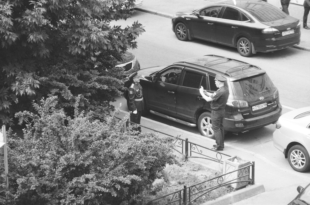 grayscale photo of man standing beside car