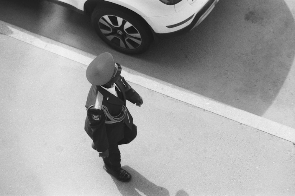 person walking on a road near a car grey-scale photography