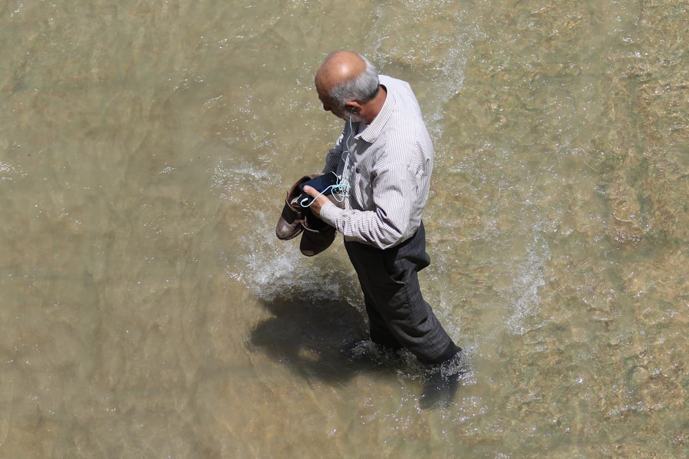 man carrying his shoes and walks at the body of water