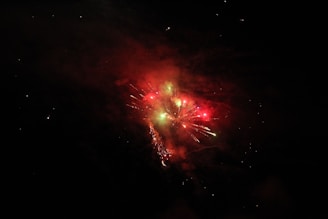 Brilliant fireworks display in a night sky, featuring vibrant bursts of red and green light. Trails and sparkles create an enchanting effect against the darkness.