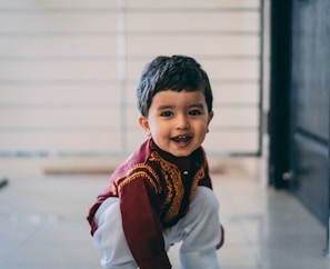 A smiling child wearing a traditional silk outfit standing beside a display of vibrant fabrics