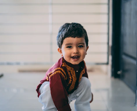 A cheerful child wearing a vibrant traditional outfit, smiling warmly against a soft cream background.