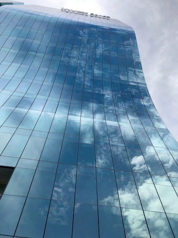 A sleek glass-fronted commercial tower reflecting the Gurgaon skyline at sunset.