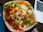 A bowl of fresh salad with leafy greens, sliced carrots, hard-boiled eggs, and roasted meat, drizzled with a creamy dressing. A laptop and a metal fork are visible nearby on a dark surface.