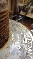 Close-up view of a metal surface with text engraved on it. The focus is on a rusty, corroded, industrial component. The text includes technical specifications, possibly related to pressure or mechanical components.