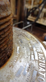 Close-up view of a metal surface with text engraved on it. The focus is on a rusty, corroded, industrial component. The text includes technical specifications, possibly related to pressure or mechanical components.