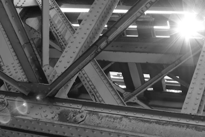 Sunlight filtering through steel girders as a crew welds a joint on a high-rise frame.