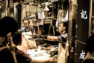 A street market scene with vendors and customers exchanging goods and money.
