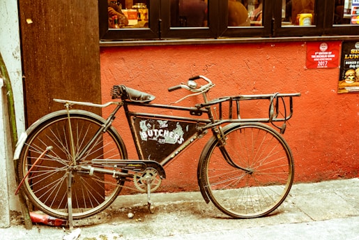 A rustic bicycle leaning against a cozy workshop wall with a small sausage hanging from the handlebar.