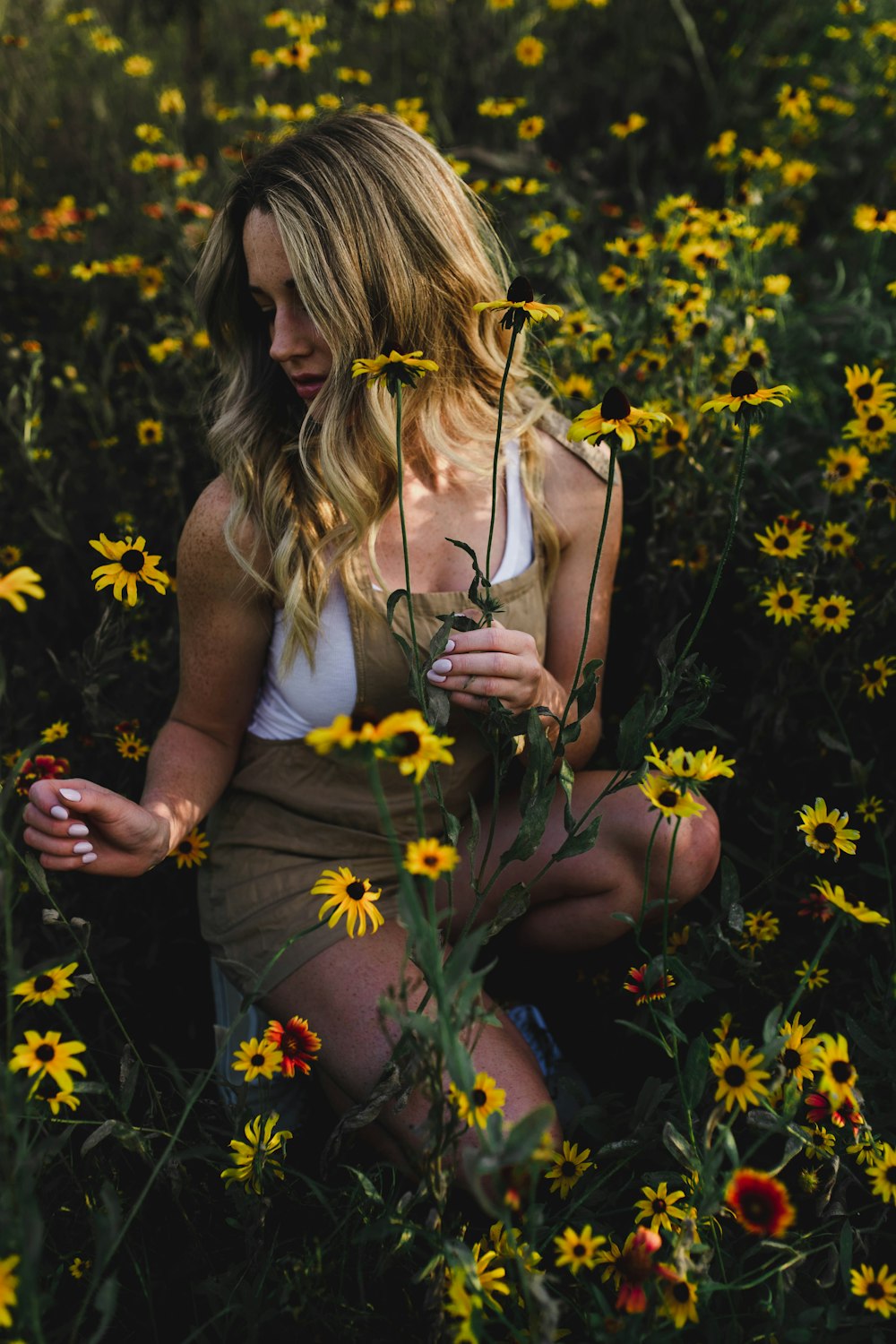 woman sitting on green grass and yellow multi-petaled flower