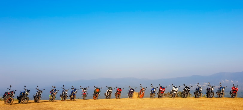 A panoramic shot of bmck motorcycles lined up on a mountain overlook at sunset.