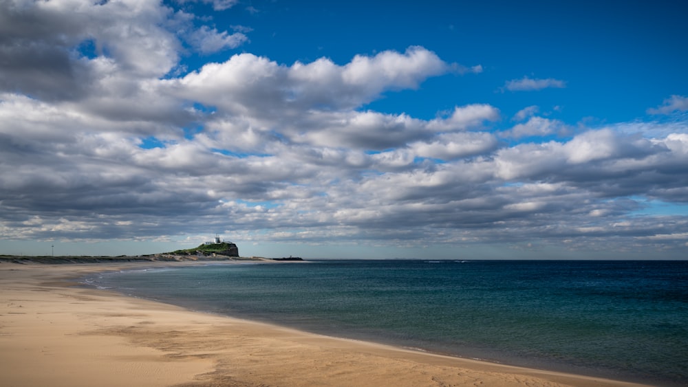 a sandy beach next to the ocean under a cloudy sky