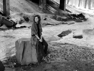 A candid shot of a thoughtful adult sitting quietly on a rock by a river.