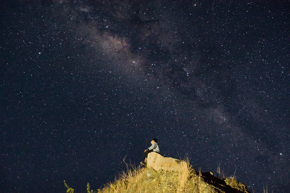 man sitting on mountain top under starry night sky
