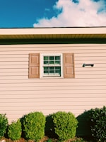 Exterior of a cozy home featuring a clean, smooth beige paint job with dark blue shutters.