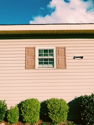 A team carefully painting a home's trim and shutters on a bright day.