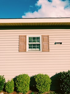 A team carefully painting a home's trim and shutters on a bright day.