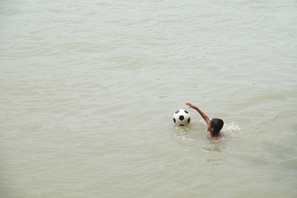 boy playing on body of water with ball