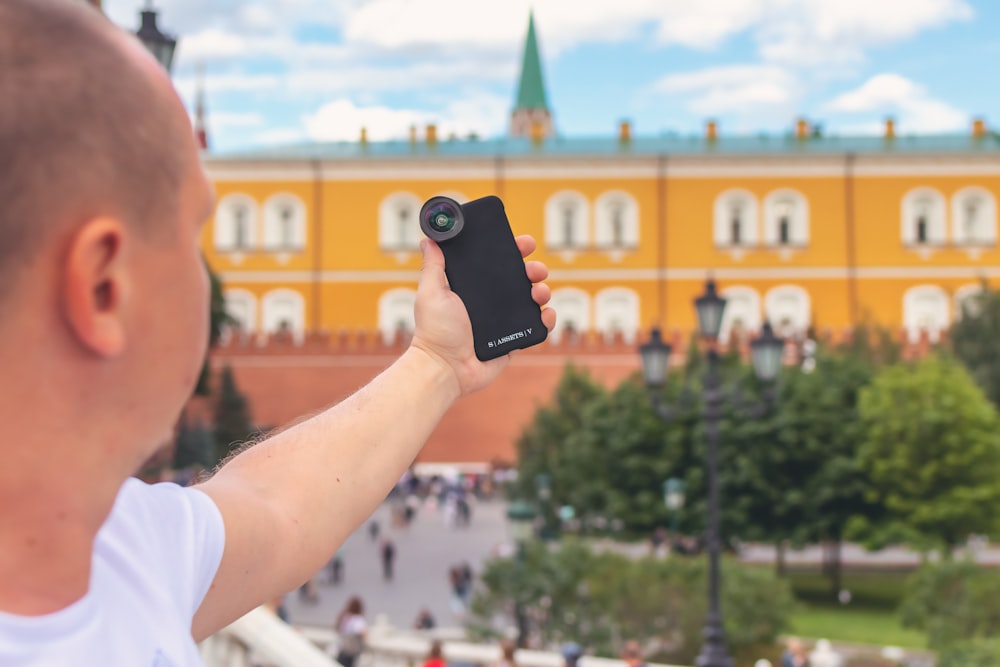 man holding phone near building and trees