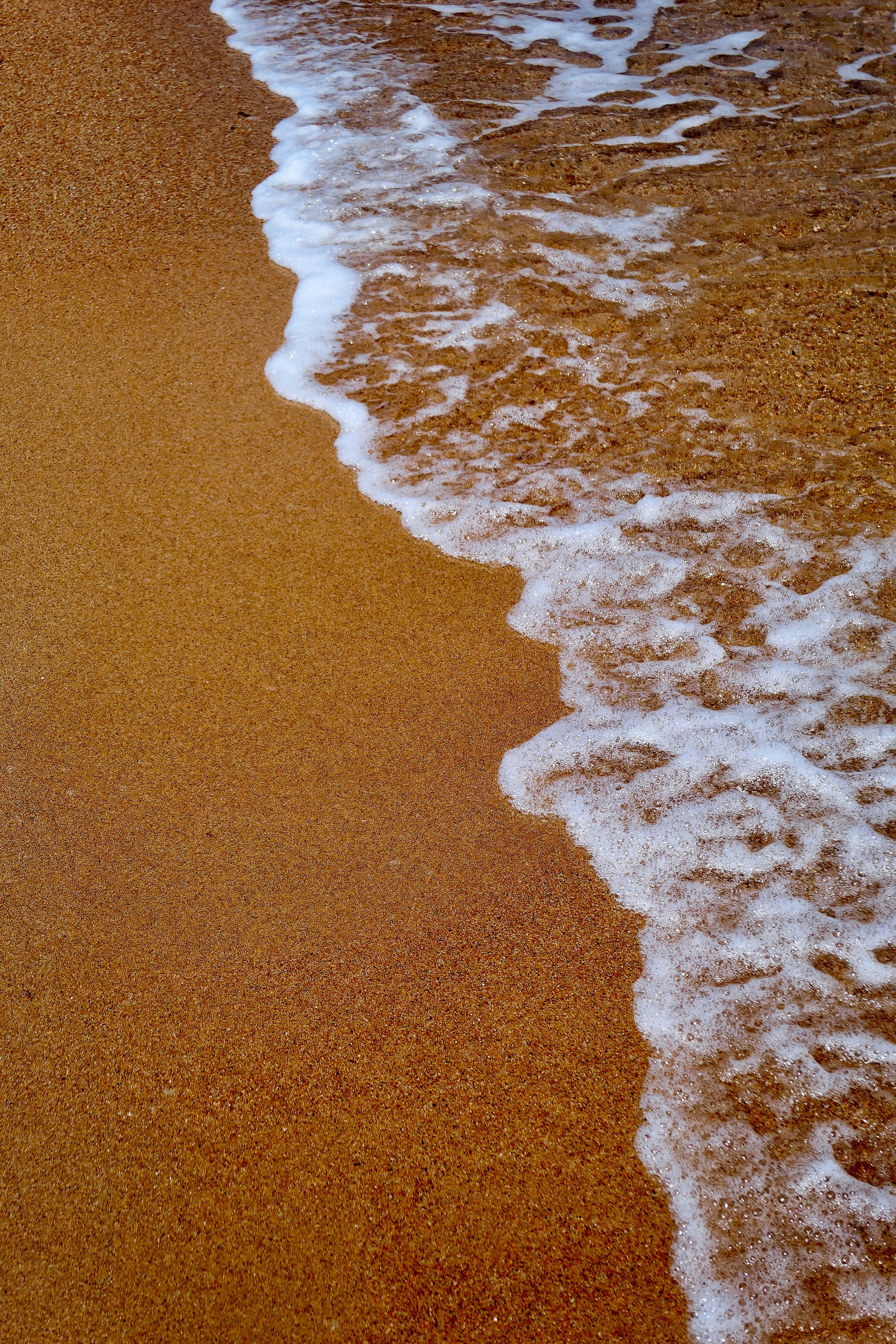 white sea foam on brown sandy beach