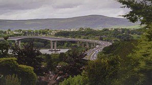 A panoramic view of a transport truck crossing a scenic bridge with lush greenery