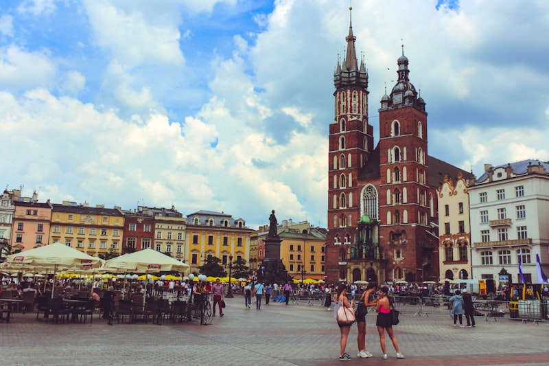 St. Mary's Basilica's twin brick towers rising over Kraków's Main Market Square, with market umbrellas and people below