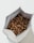 An open bag filled with roasted coffee beans, the beans are well-roasted and have a rich, brown color. The bag is positioned on a light surface with the top slightly crumpled, showing the contents inside.