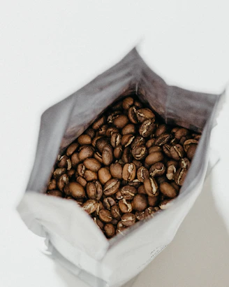 Close-up of a standup coffee pouch with rich, dark roasted beans spilling out.
