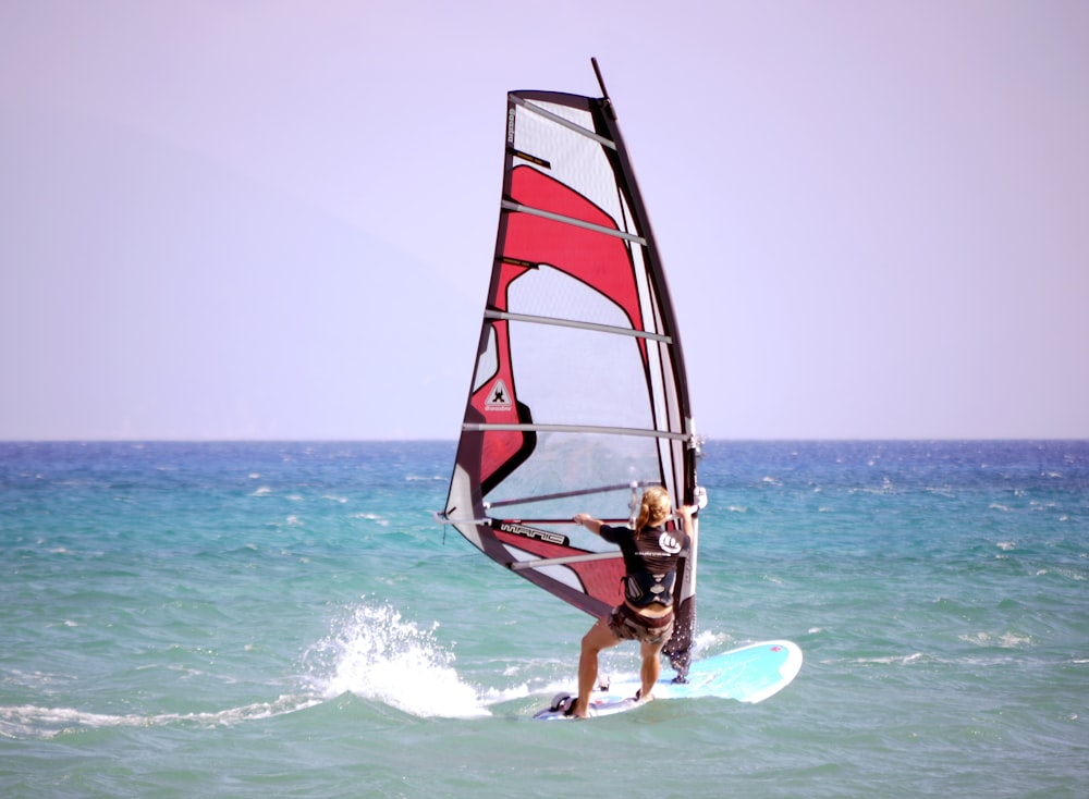 man riding sailboard under white sky