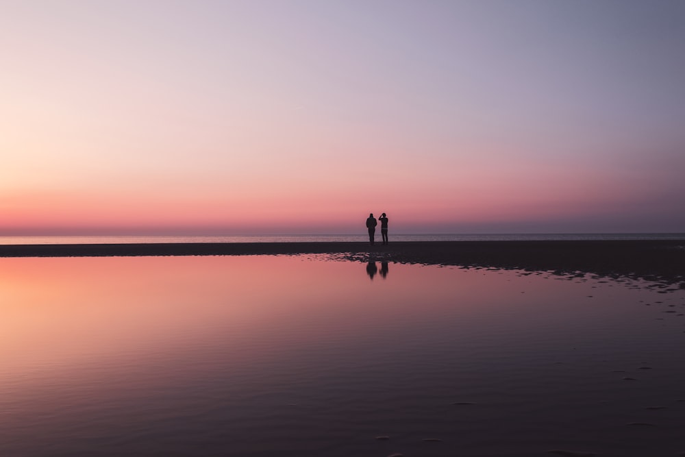 two person standing on shore near body of water