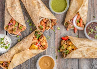 A rustic wooden table with a colorful wrap filled with chicken, veggies, and creamy sauce, styled minimally.