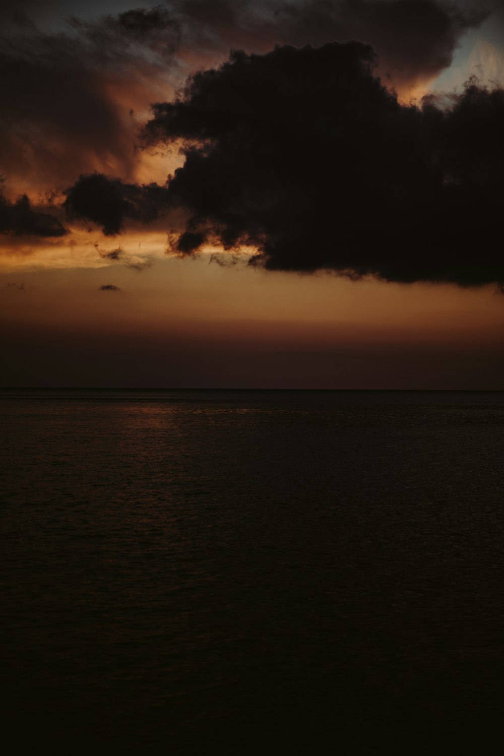 the sun is setting over the ocean with dark clouds