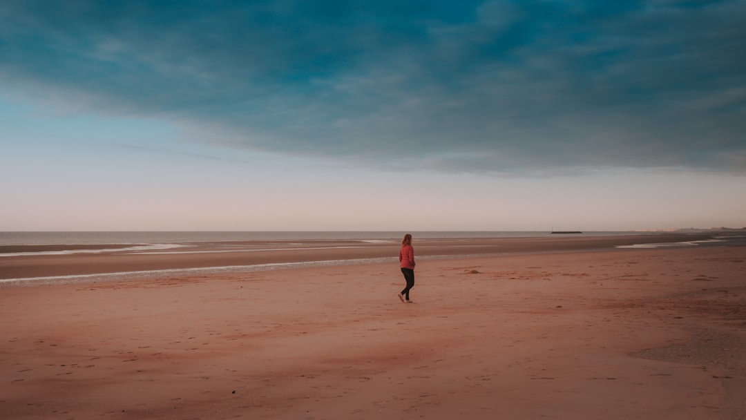 woman walking on sand beside seashore during daytime