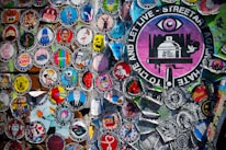 A vibrant collection of circular street art stickers with various illustrations and messages, including a prominent large sticker featuring an eye and the text 'TO LIVE AND LET LIVE - STREETART AGAINST HATE.' The stickers display a wide range of artistic styles and colorful graphics against a textured background.