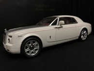A white luxury car with a sleek design, featuring silver accents and a subtle red stripe. The car is positioned at an angle, showcasing its smooth lines and large wheels against a dark background.