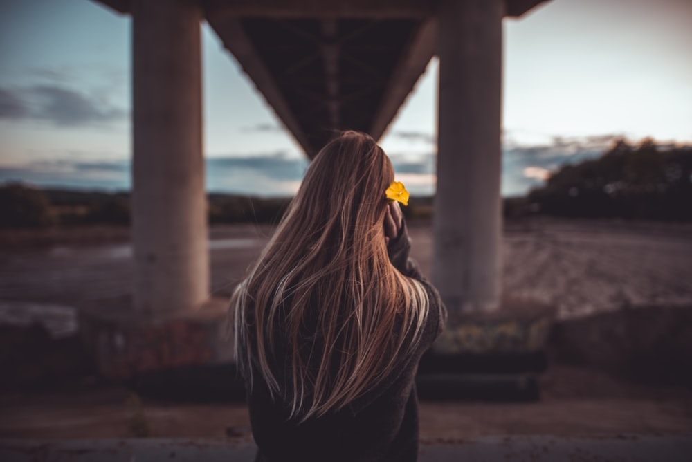 woman wearing black jacket standing under concrete bridge during golden hour