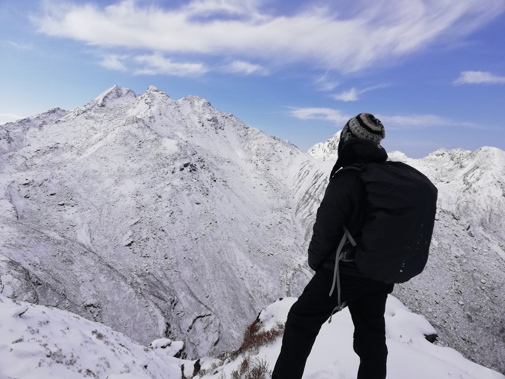 person standing on rock formation facing snow capped mountains