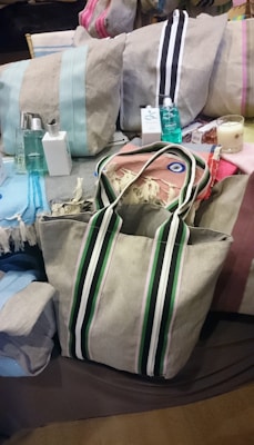 A variety of fabric bags with different colored stripes are arranged alongside toiletries, such as perfume bottles and soap. There is also a decorative evil eye charm and a candle.